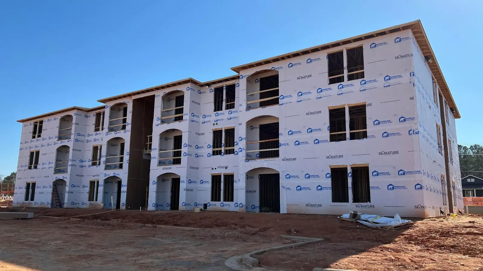 A three-storey apartment building under construction, sheathed and windowed, seen from the site road