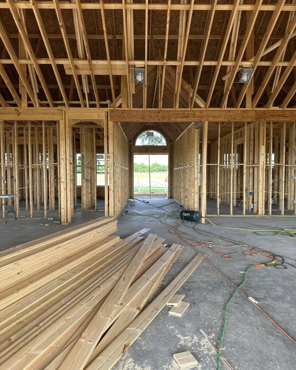 Interior of a house at framing stage, stud walls and a framed archway with lumber stacked on the slab