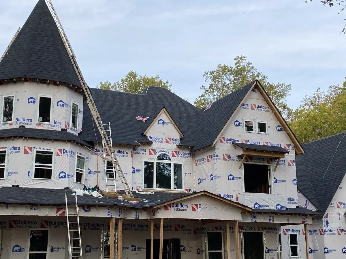 A large two-storey home under construction with a turret and steep roof pitches, ladders against the wall